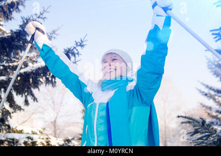 Attraktive lächelnde Blondine mit Skistöcken in den Händen, genießt einen Ski laufen Im Winter Wald Stockfoto