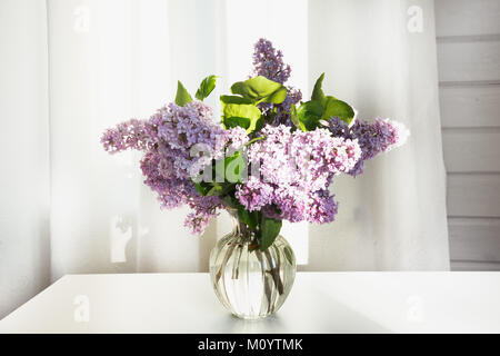 Einen Strauß mit frischen Flieder in einem schönen Glas Vase auf einem weißen Tisch in einem Haus im Dorf. Stockfoto