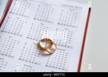 Die Planung einer Hochzeit in 2018. Kalender von 2018 und zwei Trauringe auf weißem Hintergrund Stockfoto