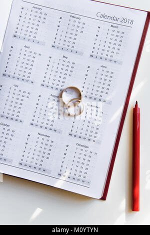 Die Planung einer Hochzeit in 2018. Kalender von 2018, zwei Ringe und ein Stift auf weißem Hintergrund Stockfoto