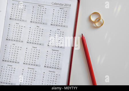 Die Planung einer Hochzeit in 2018. Kalender von 2018, zwei Ringe und ein Stift auf weißem Hintergrund Stockfoto