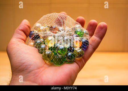 Hand hält bunte Glasmurmeln im Netz Stockfoto