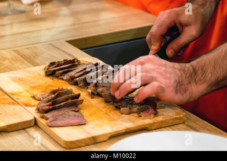 Koch Hände schneiden Steaks mit Messer auf Schneidebrett. Warme Gerichte Konzept Stockfoto