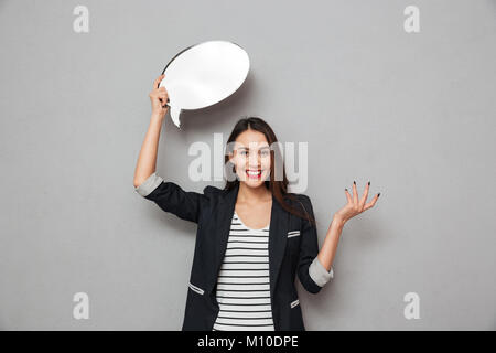 Glücklich überrascht Asian Business woman holding leere Sprechblase, und wenn man die Kamera über grauer Hintergrund Stockfoto