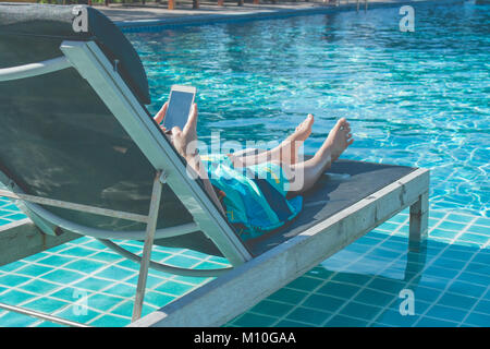 Liegende Frau in Liege und Ihr Smartphone spielen neben dem Pool. Stockfoto