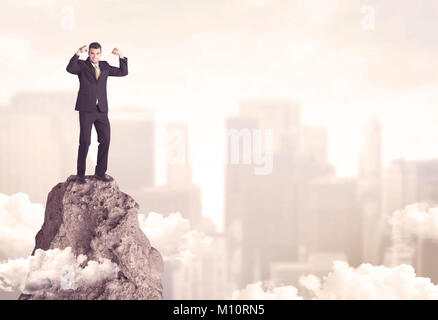 Eine professionelle Sieger business Person, die auf einem gefährlichen Berg über der Stadt scape mit Wolken Konzept Stockfoto