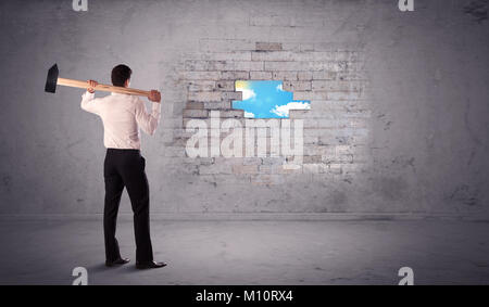 Business Mann schlagen grungy Ziegelmauer mit Hammer Stockfoto