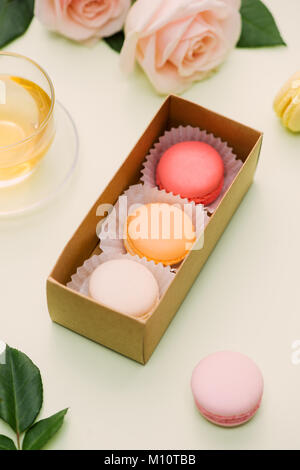 Bunte Makronen und rosa Blüten mit Tee auf hellgrün. Süße macarons in Geschenkbox. Ansicht von oben Stockfoto