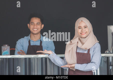 Asiatische muslimischen Kellner Begrüßung des Kunden an Ihr neu eröffnetes Cafe zu kommen Stockfoto