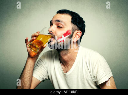 Lustig sport Fan mit Fahne gemalt auf Gesicht Bier trinken. Stockfoto