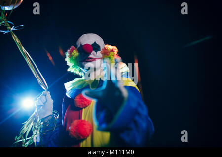 Fotos von lächelnden Clown mit Luftballons gegen den Hintergrund von brennenden Laternen in der Nacht auf der Straße Stockfoto