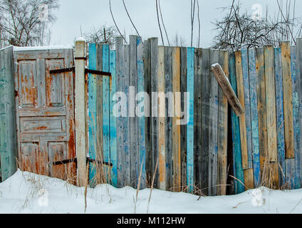 Farbige alten hölzernen Zaun und eine alte Tür eines verlassenen Hauses auf einem Hintergrund von Schnee und Bäume Stockfoto