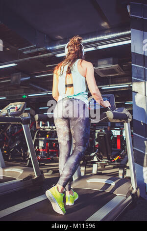 Thema Sport und Gewichtsabnahme. Beine einer Jungen starke Frau in Hellgrün Sneakers, Hosen und Kopfhörer auf dem Simulator, an der Turnhalle. Prehe Stockfoto