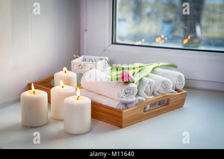 Gerollte Handtücher auf ein Fach neben dem brennenden Kerzen und ein Blumenstrauß aus Tulpen in der Spa Salon Stockfoto