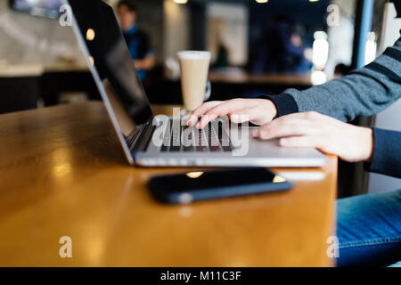 Casual business Mann Arbeiten am Laptop mit Buch, Notebook, mobile Smartphone und Tasse Kaffee am Tisch im Café oder im Home Office Stockfoto