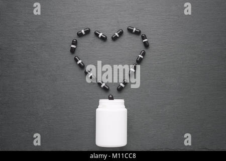 Schwarz Ergänzung Kapseln in Herz Form angeordnet sind von weiße Flasche gegossen. Ansicht von oben, flach, kopieren. Medizin, Gesundheitswesen Konzept Stockfoto