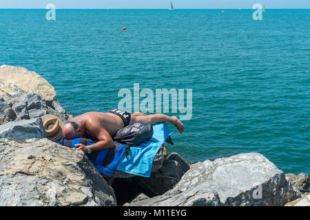 Mann, Sonnenbaden auf den Felsen am Strand von Viareggio, Toskana, Italien. Stockfoto