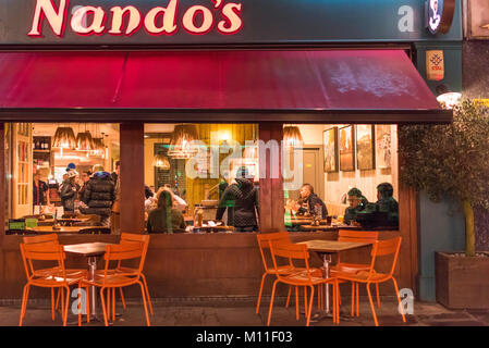 Nando's in der Nacht. Kunden im Restaurant sitzen in der Abenddämmerung in Canterbury High Street, Kent, Großbritannien fällt. Stockfoto