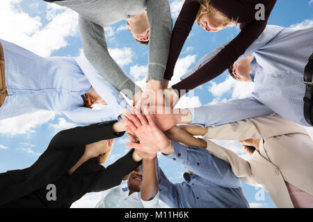 Low Angle View Studenten Stapeln ihre Hände gegen bewölkter Himmel Stockfoto