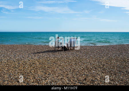 Alte Paar setzte sich auf Liegestühlen am Brighton Beach mit Blick auf das Meer Stockfoto