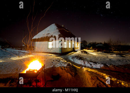 Heiße Grill Feuer auf altes Haus Hintergrund mit Strohdach im winter nacht Stockfoto