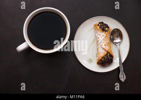 Italienische cannoli mit Chocolate Chips auf weißen Teller und Tasse auf schwarzem Hintergrund Stockfoto