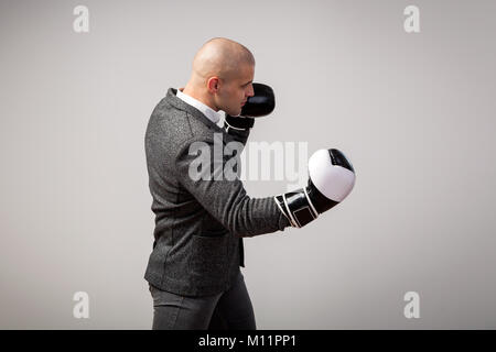 Junge glatzköpfige Mann, zuversichtlich business Mann im weißen Hemd, grauen Anzug und Boxhandschuhe ein Aufwärtshaken, Boxen auf weißem Hintergrund isoliert, Seitenansicht Stockfoto