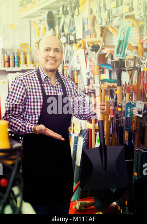 Professionelle senior Verkäufer mit Garten Werkzeuge in Gebäude store Stockfoto