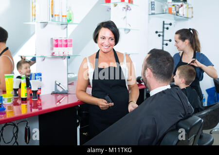 Positive reife Frau Friseur zu männlichen Klienten im Beauty Salon chatten Stockfoto