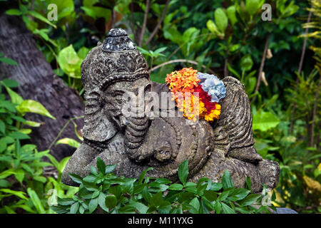 Indonesien, Insel Bali, in der Nähe von tejakula Dorf, Gaia Oasis Resort. Statue des hinduistischen Gottes Ganesha mit Blume im Garten. Stockfoto