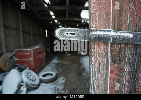 Alte und verwitterte Tür Haspe durch Frost mit alten, verlassenen Garage im Hintergrund Stockfoto