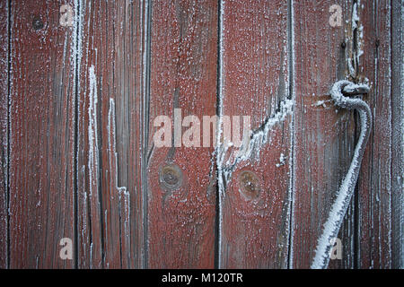 Alte und verwitterte Tür Haspe durch Frost gegen rote Holz- und verwitterte Wand abgedeckt Stockfoto