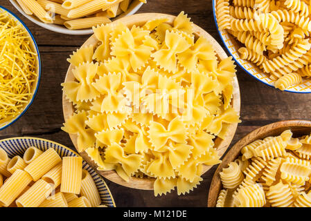 Verschiedene Arten von Rohstoffen, wie z. B. Pasta Fusilli, Penne Rigate, Radiatori, Farfalle, Mezzi Rigatoni und Eiernudeln in Schalen auf Holz rustikale Hintergrund Stockfoto