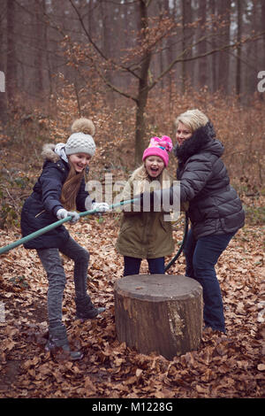Zwei Kinder und eine weibliche Erwachsene, ziehen Tauziehen auf einem Seil in Wäldern Stockfoto