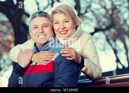 Positive Mann und Frau umarmen einander sitzen auf einer Parkbank Stockfoto