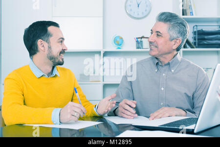 Junger Mann und Mitarbeiter der Bank zu diskutieren und Kreditvertrag im Büro anmelden Stockfoto