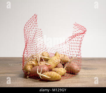 Ein Beutel mit alten Kartoffeln ab dem holztisch vor weißem Hintergrund zu Keimen Stockfoto
