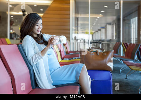 Frau im Flughafen Lounge im Stuhl sitzend durch das Fenster schaut auf ihre Uhr warten auf Ihren Zeitplan zu fliegen Stockfoto