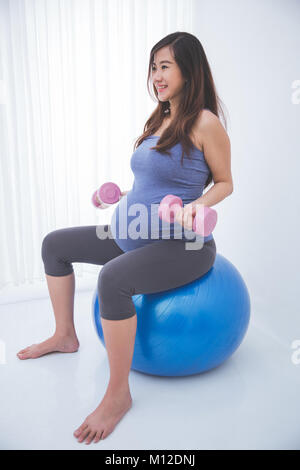 Das Portrait einer schönen asiatischen schwangere Frau, Übung mit Yoga ball, Holding barbell in jedem Hände Stockfoto