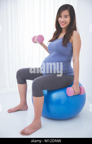 Schwangere Frau, Übung mit Yoga ball, Holding barbell in jedem Hände Stockfoto