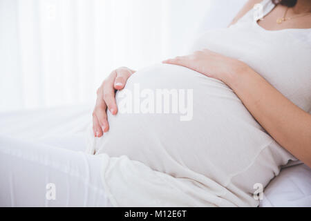 Eine Nahaufnahme portrait einer schwangeren Bauch gelehnt auf dem Bett Stockfoto