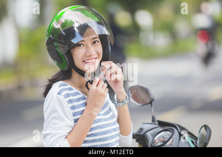 Glückliche Frau ihrem Motorrad Helm Befestigung in der Stadt. Stockfoto