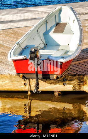 Kleine rote Motorboot auf einem hölzernen Dock mit Spiegelungen im Wasser. Rot, Weiß und Blau. Stockfoto