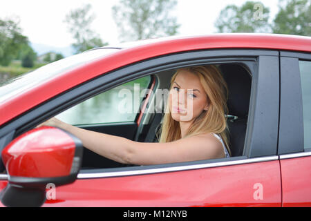 Junge, attraktive blonde Mädchen in neuen roten Auto, die die Stirn runzelt, mit einem Gesichtsausdruck Wirklich? Erzählen Sie mir nicht... Stockfoto