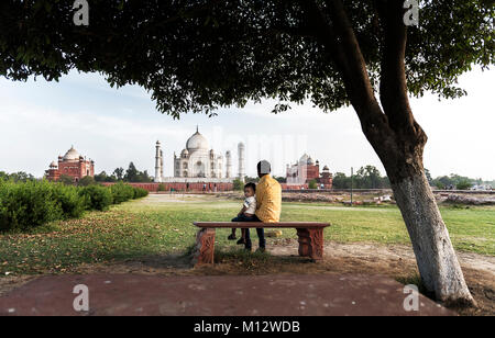Zwei Jungen sitzen unter Bäumen und genießen die herrliche Aussicht auf den Taj Mahal, Agra, Indien Stockfoto