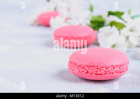 Rosa und Lila Makronen auf einem grauen Tabelle mit rosa und weißen Blüten umgeben Stockfoto