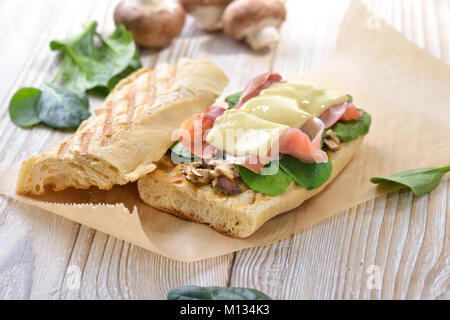 Street Food: heiße Panini mit Spanischer Serrano Schinken und junge spinatblätter gekrönt mit geriebenem Käse auf einem hölzernen Hintergrund serviert. Stockfoto