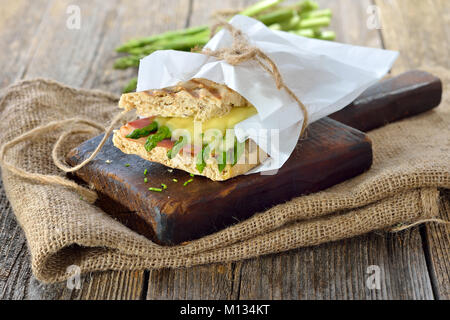 Street Food: heiße Panini mit Schinken und grünem Spargel überbacken mit geriebenem Käse auf einem hölzernen Hintergrund serviert. Stockfoto