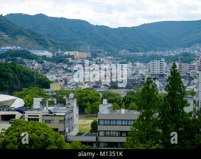 Vogelperspektive der Stadt Nagasaki mit zwei Gebäuden und Bäumen in den vorderen und den Bergen im Hintergrund. Stockfoto