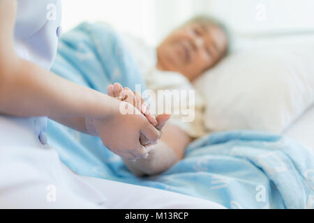 Krankenschwester sitzen auf einem Krankenhausbett neben eine ältere Frau helfende Hände, die Altenpflege Konzept Stockfoto